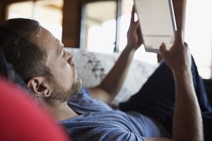 Man laying on sofa using digital tablet